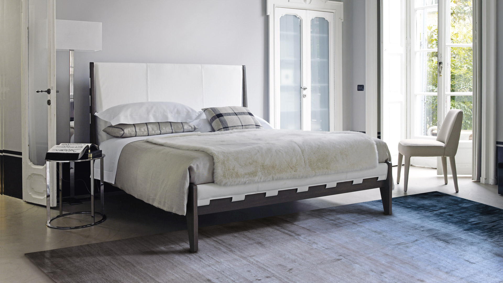 Blue-gray rug in a bedroom with white upholstered bed and classic wall paneling