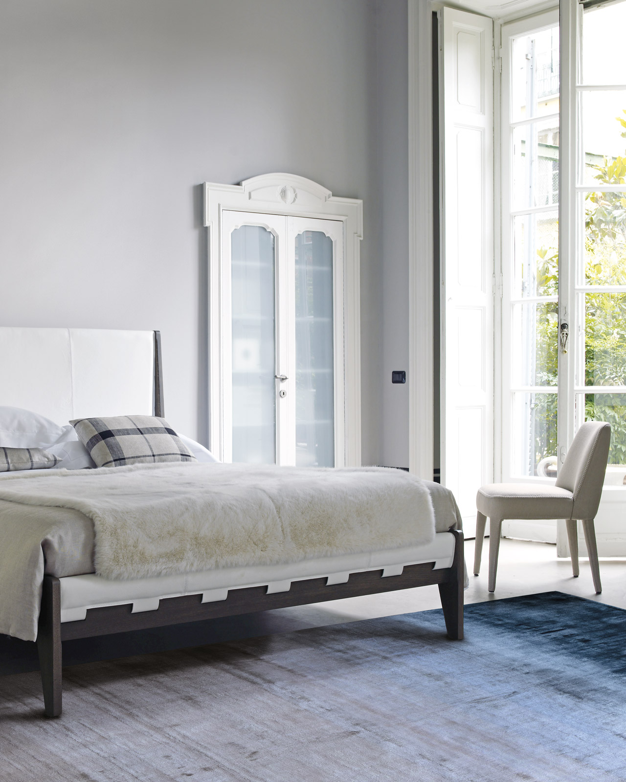 Blue-gray rug in a bedroom with white upholstered bed and classic wall paneling