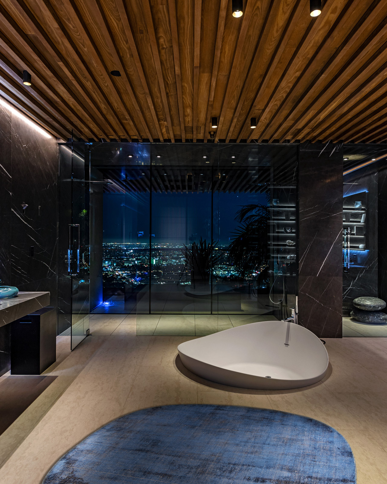 Round light-blue rug in a design bathroom with dark marble and freestanding tub